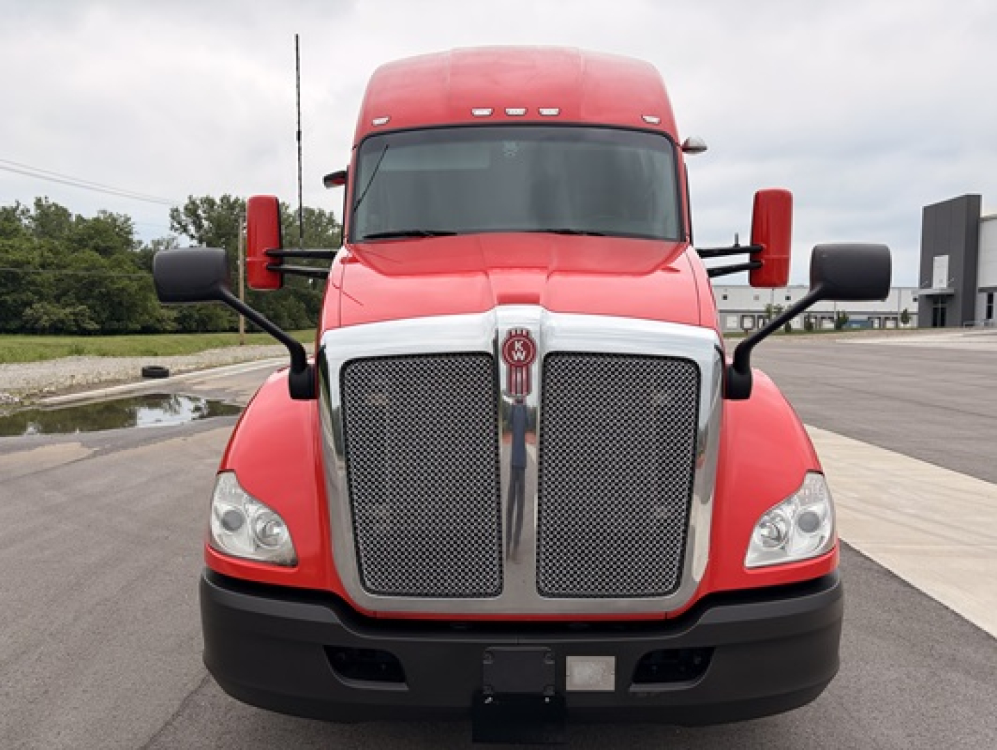 Kenworth T680 front view showing large chrome grille, red cab, black bumper, and white headlight surrounds.