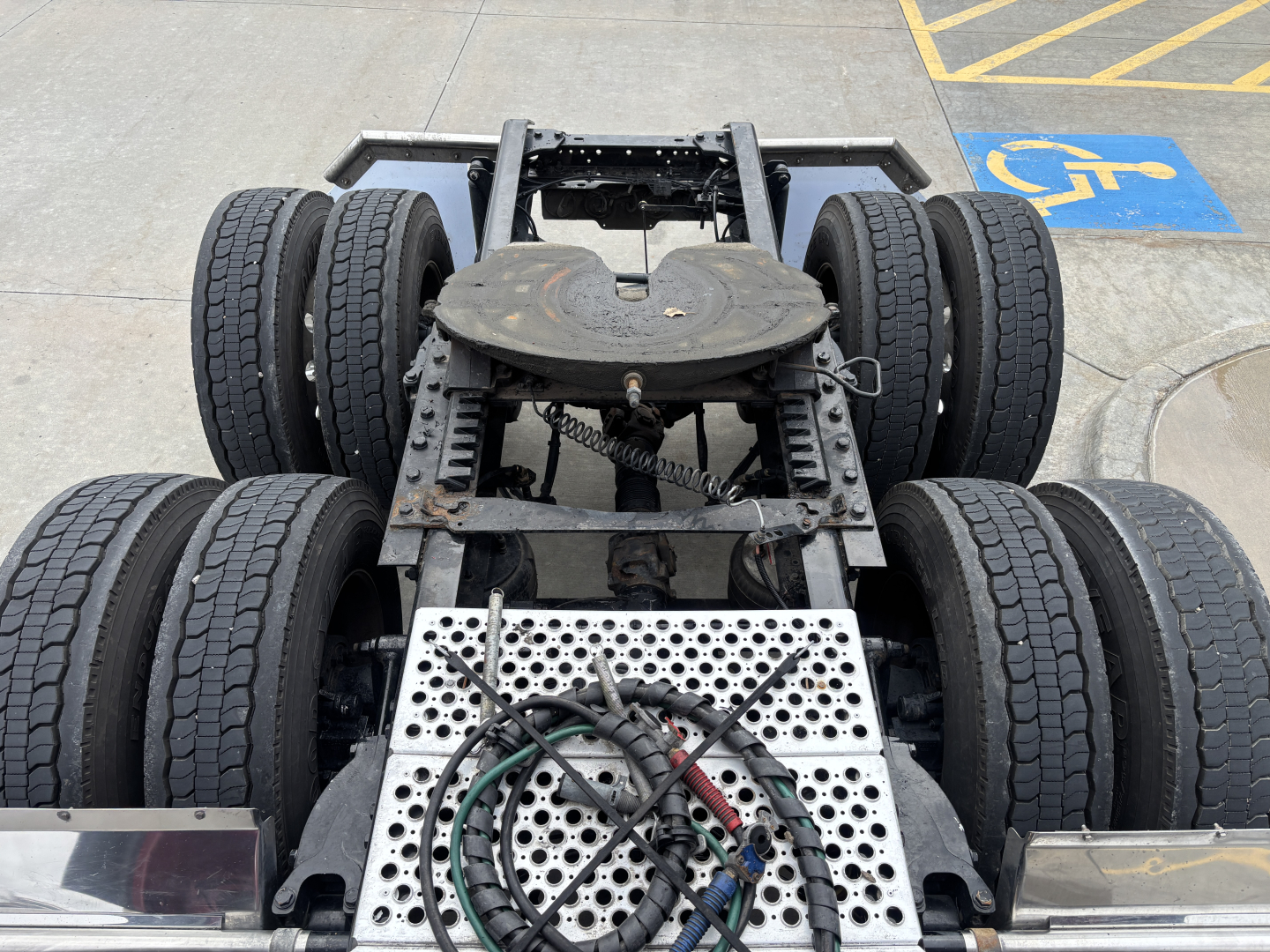 Kenworth W900L chassis with six wheels visible, metal perforated platform, hoses, and drivetrain area.