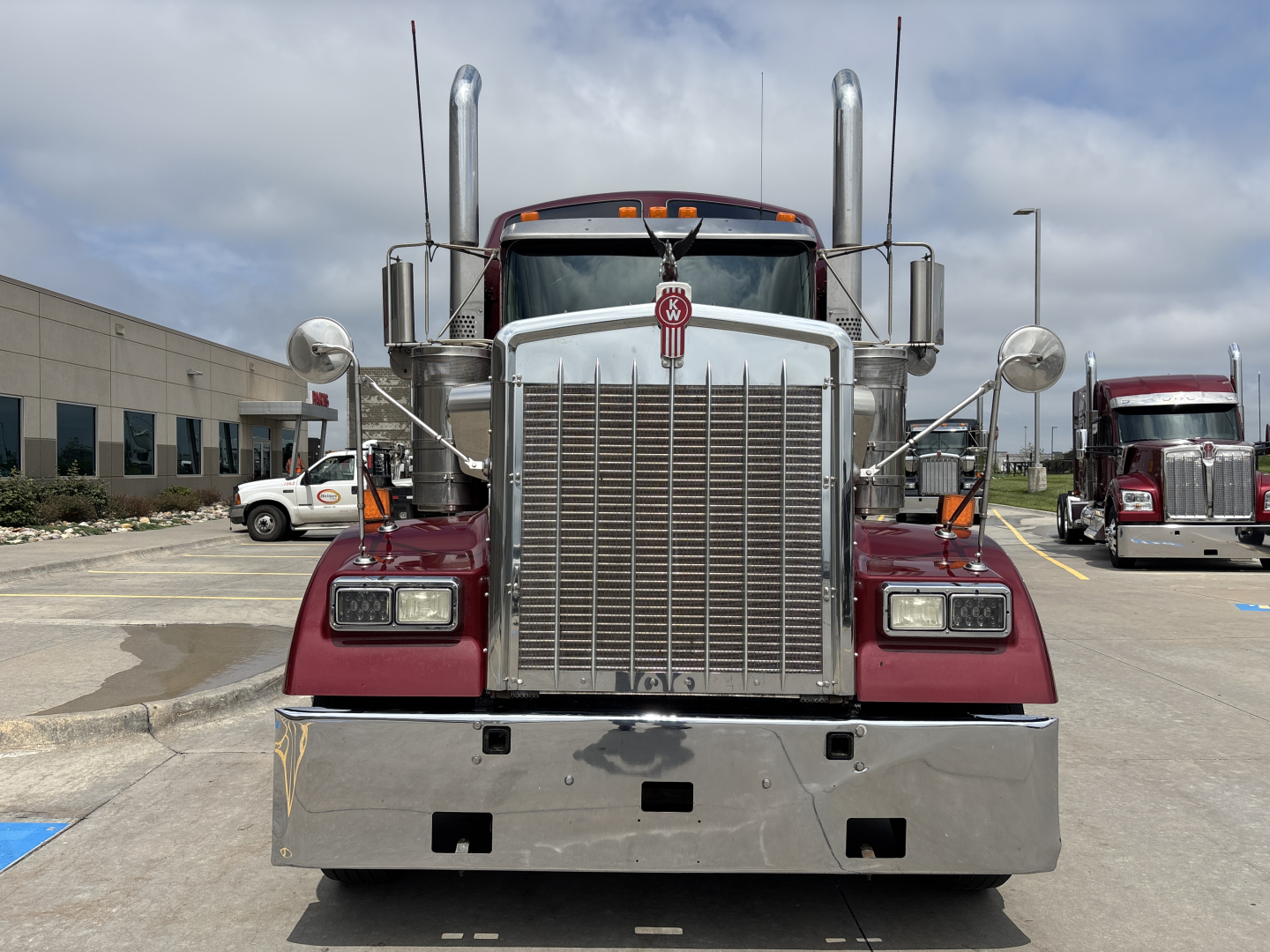 Kenworth W900L front view showing large chrome grille, two tall exhaust stacks, round mirrors, and bumper; front badges and headlights visible.
