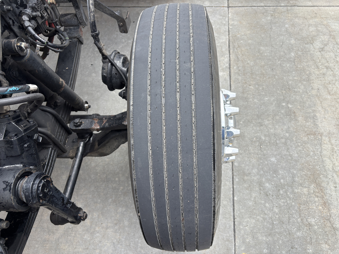 Rear wheel/tire assembly of a Kenworth W900L tractor showing large single-drive tire with visible tread wear and metallic wheel hub studs.