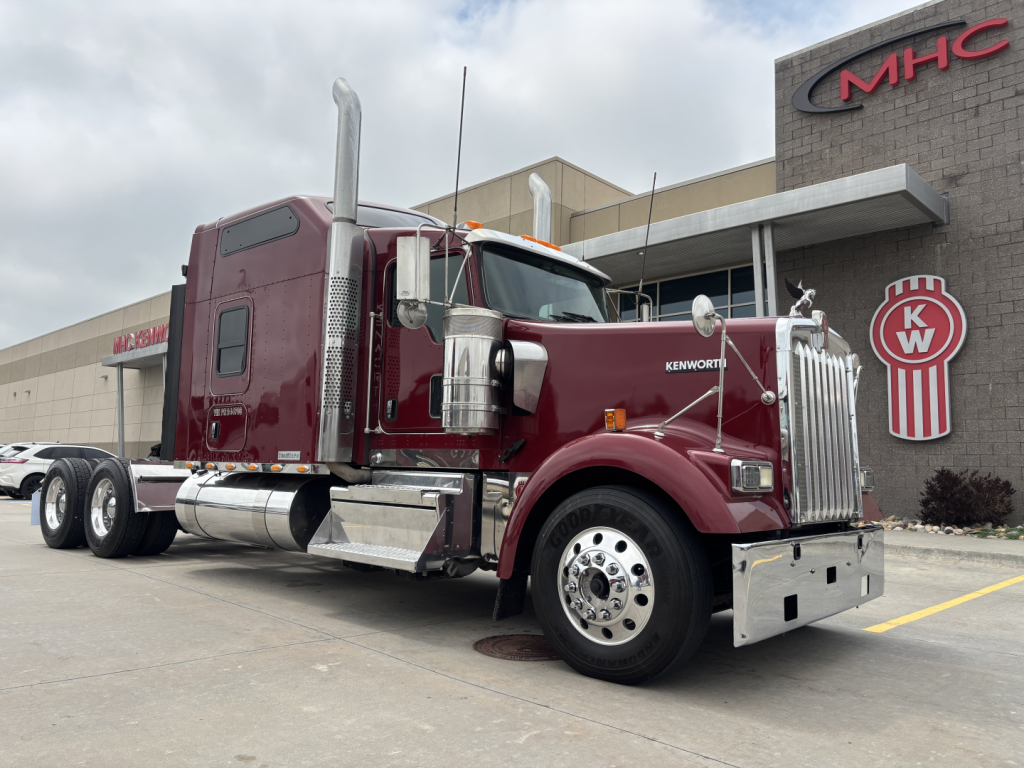 Kenworth W900L truck in maroon color parked outside dealership with chrome exhaust stacks and Peterbilt-? style grille?