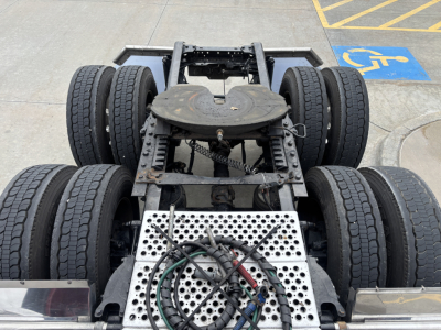 Kenworth W900L chassis with six wheels visible, metal perforated platform, hoses, and drivetrain area.