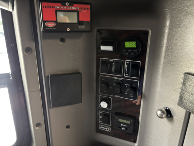 Kenworth W900L dash panel showing gauge, switches, and digital display. UPS-style control module present with various switches and a small digital clock. 