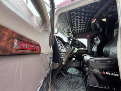 Kenworth W900L truck interior view showing driver seat, steering wheel, and Kenworth badge on door panel.