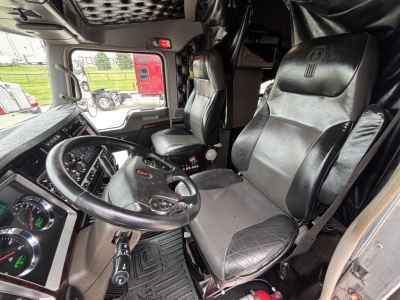 Kenworth W900L truck interior showing steering wheel, driver seat, and dashboard view with black leather seats and controls.