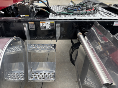 Kenworth W900L undercarriage showing steps, fuel lines, and chassis with access panels and metal tubing.