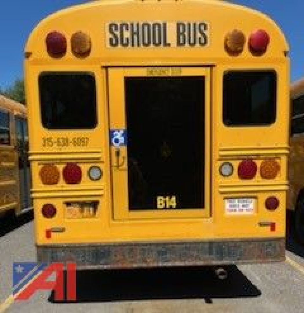 Rear of a yellow school bus with wheelchair lift door open, 'SCHOOL BUS' lettering, red and amber lights, bus number plate B14, and reflection on rear bumper.