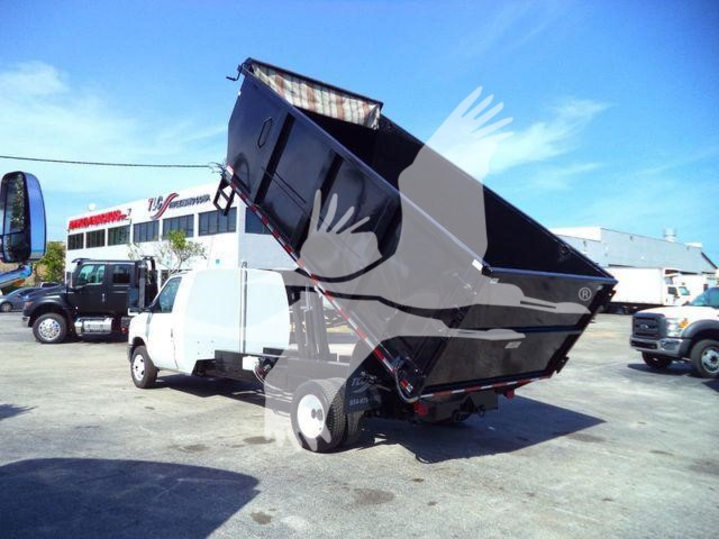 Ford E450 dump truck with dump bed raised, side view showing hydraulic mechanism and rear wheels in a yard.