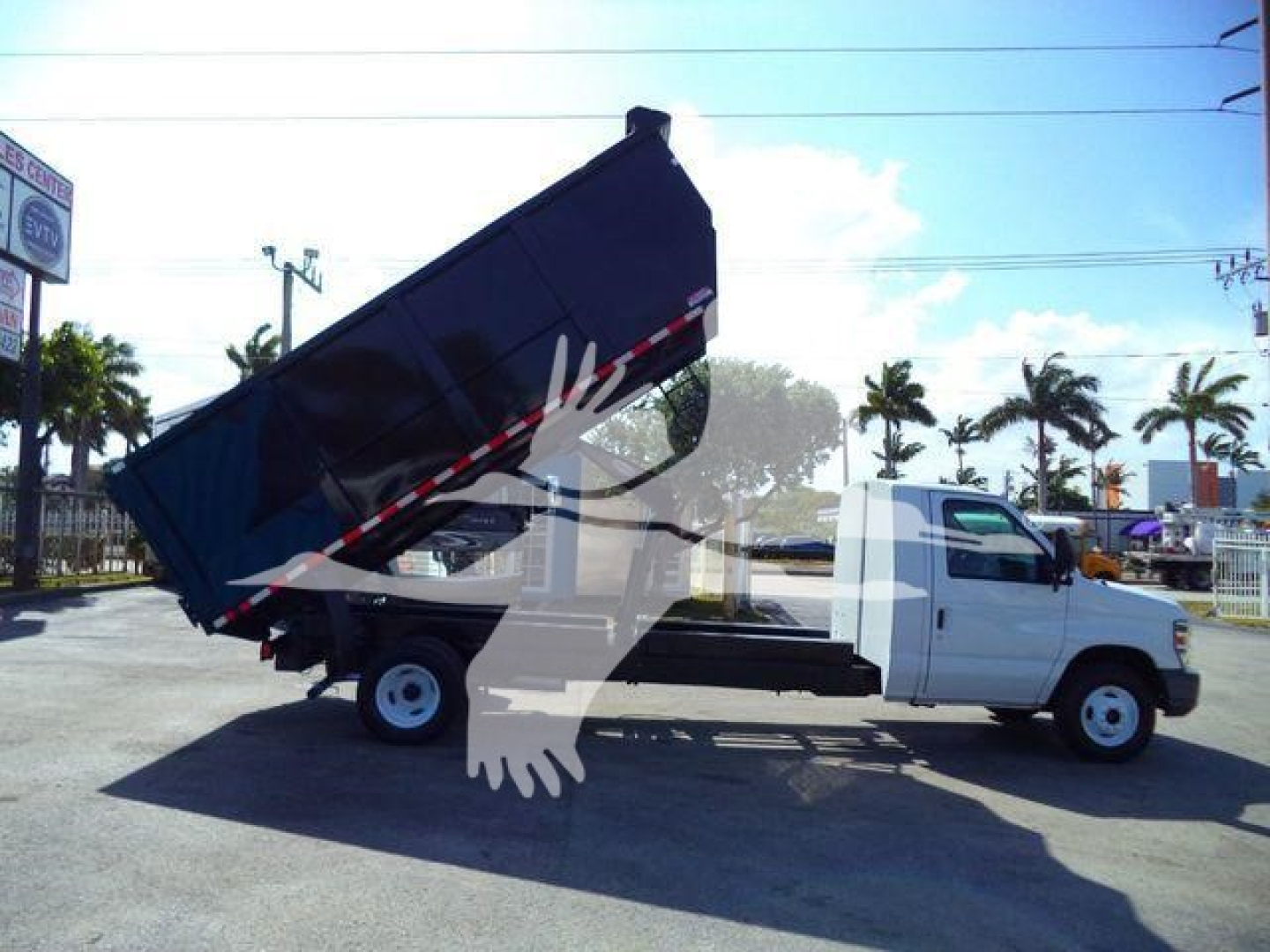 Truck bed tilted dump body on a white Ford E-450 chassis cab dump truck, mid-angled view showing rear wheels and hydraulic elevation.