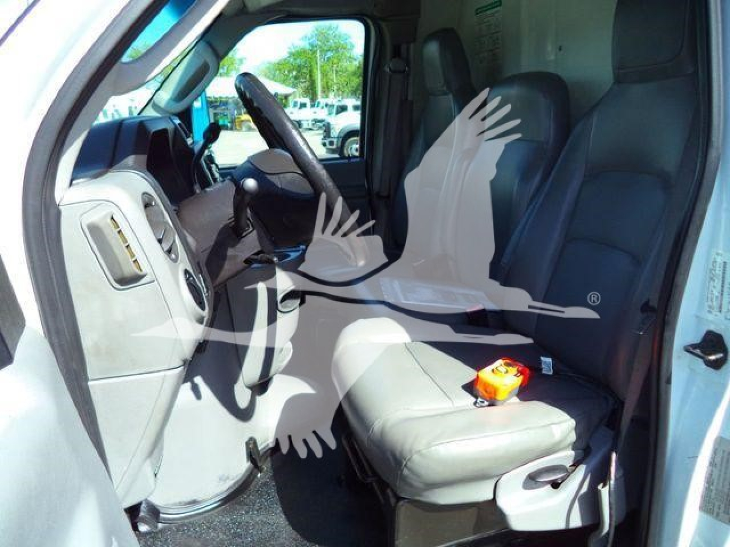 Ford E-450 cargo van interior showing driver and passenger seats with steering wheel and dashboard. Passenger seat has orange device on it.