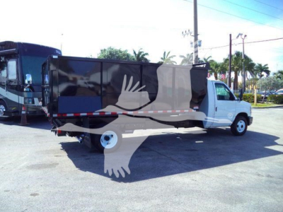Truck bed side view of a 2011 Ford E-450 dump truck with a black cargo bed and white cab, stock number T57118 PB, in-service used condition.