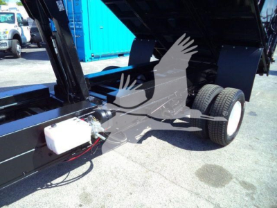 Truck bed of a 2011 Ford E450 dump truck showing hydraulic system and white reservoir with hoses.