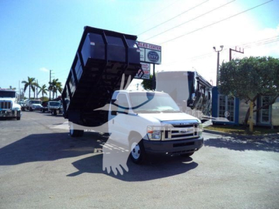 Ford E450 tow truck with a raised dump bed in a vehicle lot showing front and driver side view.