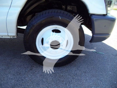 Truck wheel of a 2011 Ford E450 dump truck showing white steel rim and tire; front fender and bumper visible.