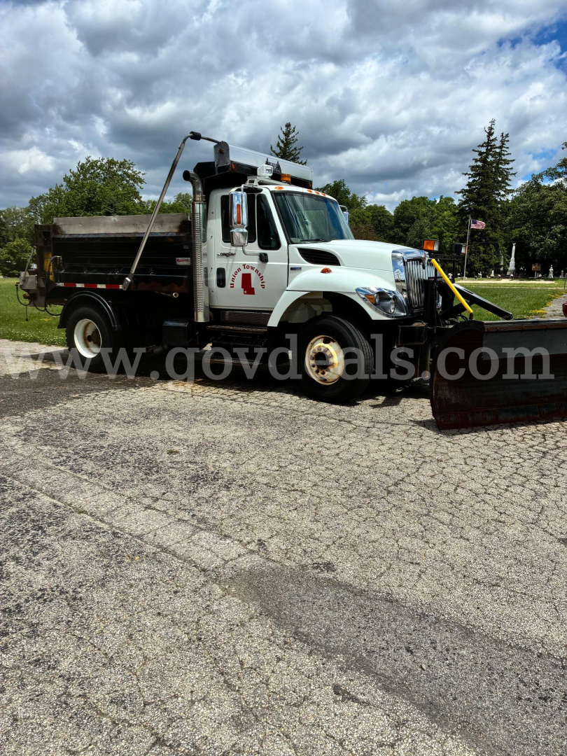 Dump truck with snowplow attachment in front, white International 7400, side view with dump bed and equipment, used vehicle.