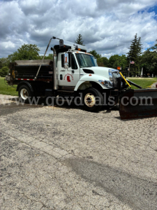 Dump truck with snowplow attachment in front, white International 7400, side view with dump bed and equipment, used vehicle.