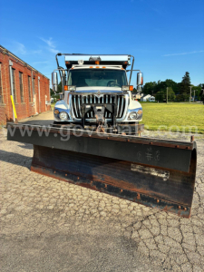 Truck front view with snow plow attachment, International 7400 dump truck, chrome grille, large headlights, side mirrors, hood ornament, and plow blade in foreground.