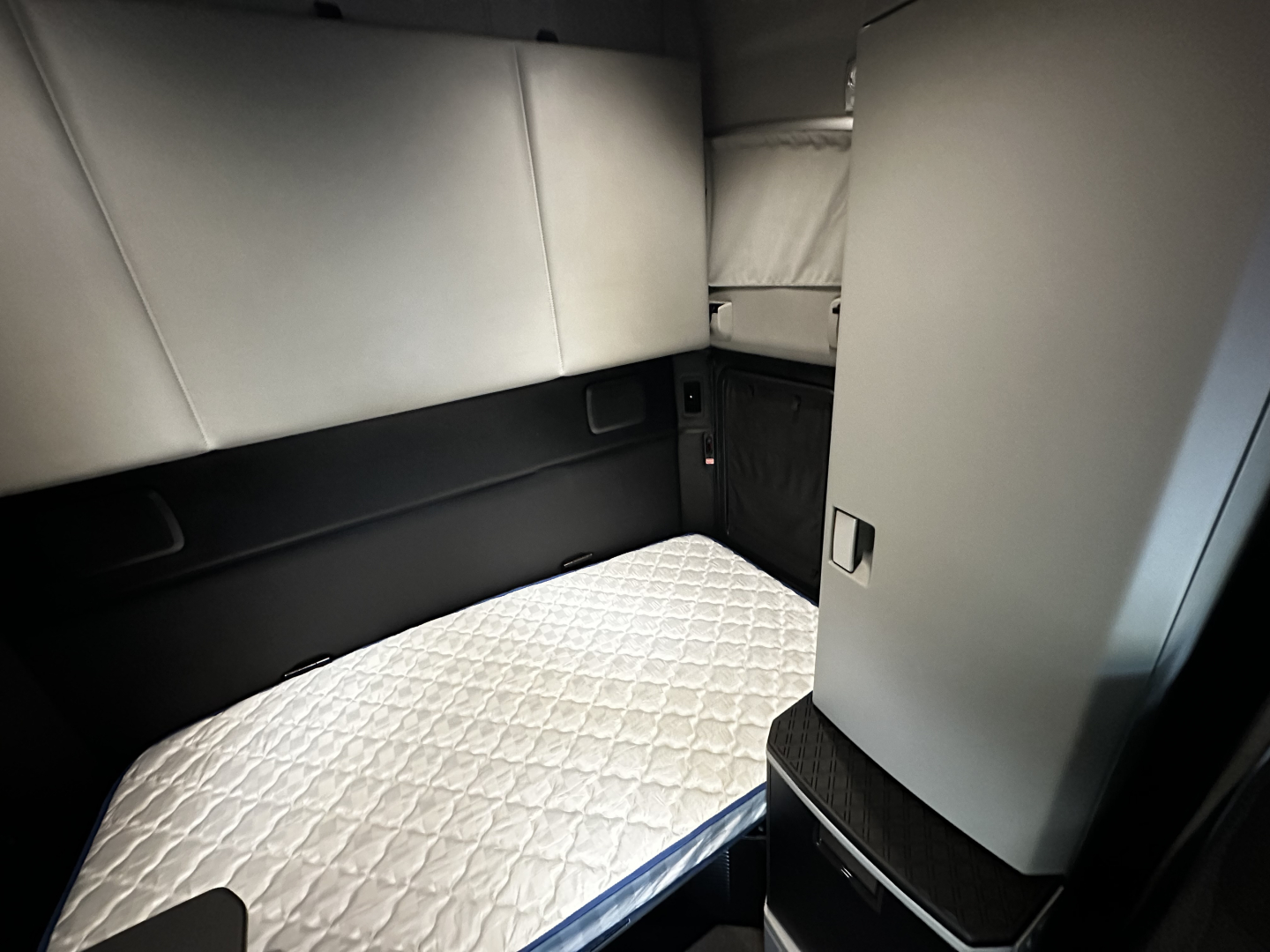 Kenworth T680 sleeper cab interior view with quilted mattress and side storage panels.
