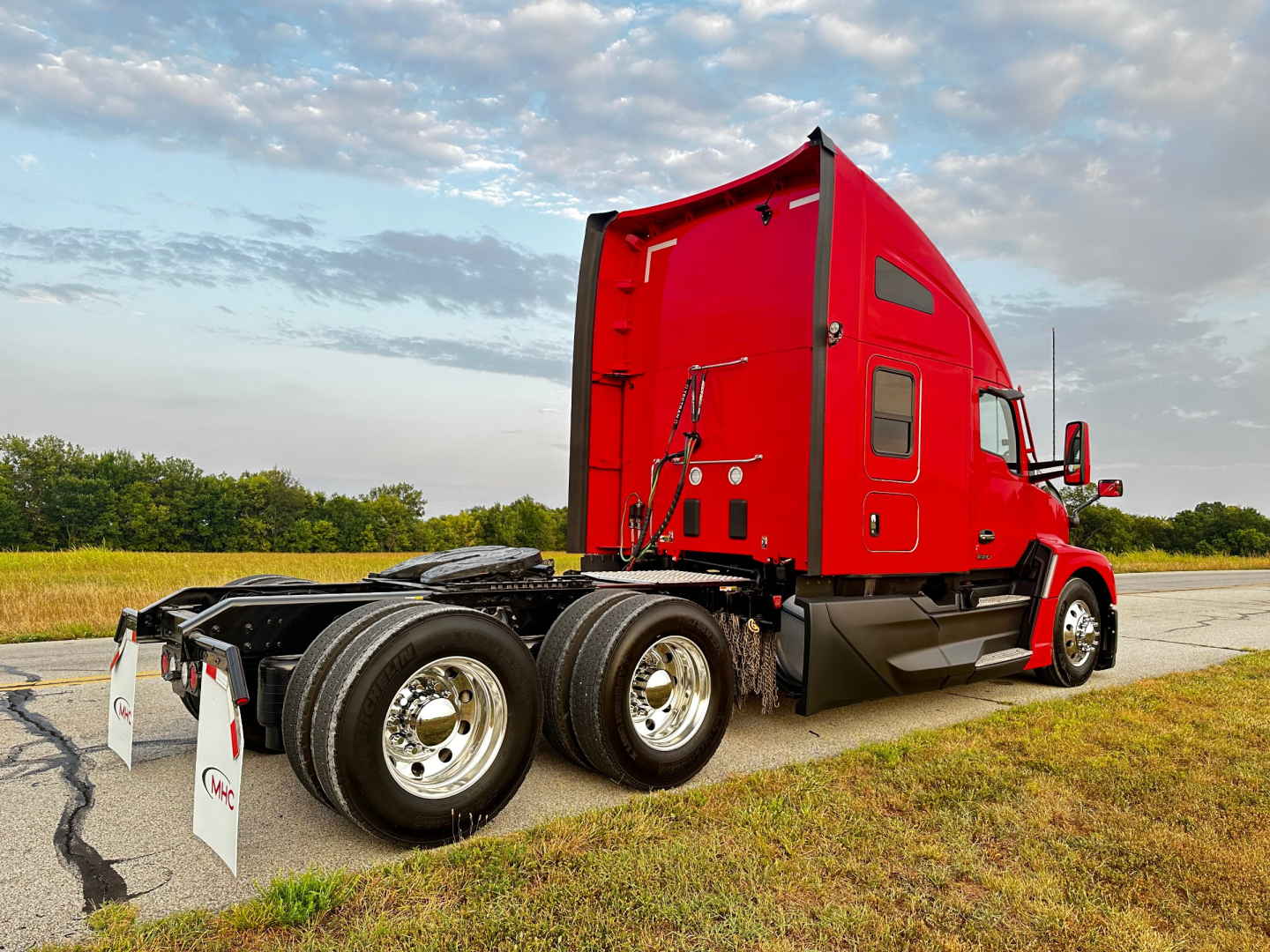 Kenworth T680 tractor with red sleeper cab, dual rear axles, and chrome wheels visible in a roadside setting.