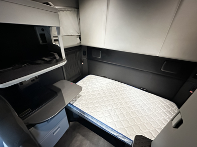 Cab interior of a Kenworth sleeper with a quilted mattress in the bunk area and storage compartments on the left. 