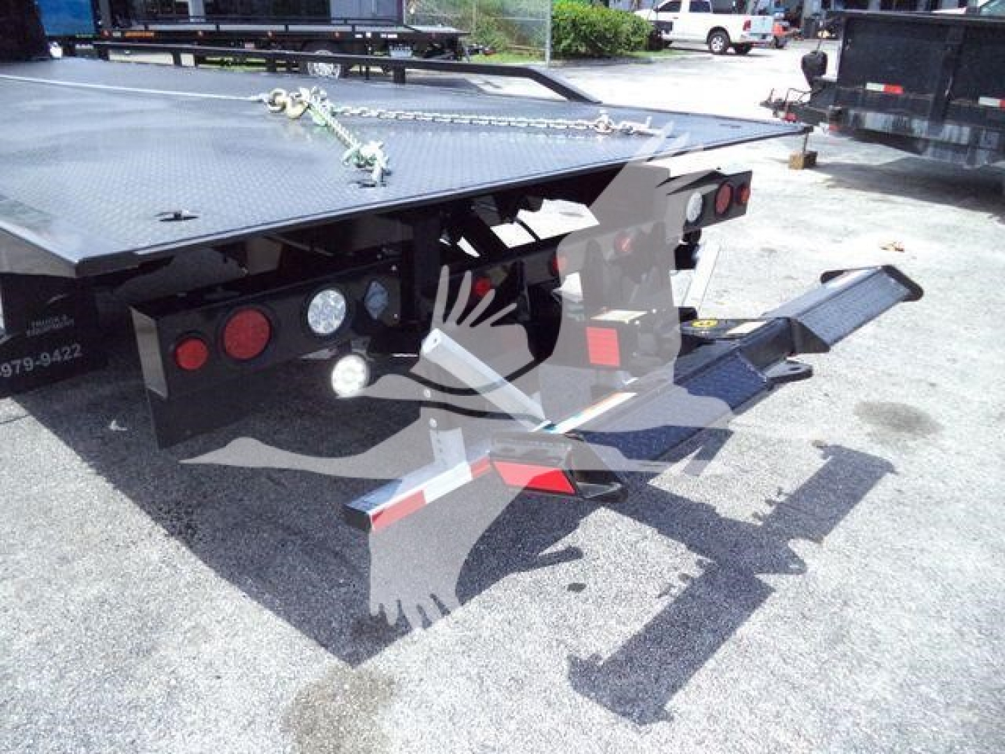 Flatbed rollback trailer showing rear ramp and taillights with chains and reflective markings.