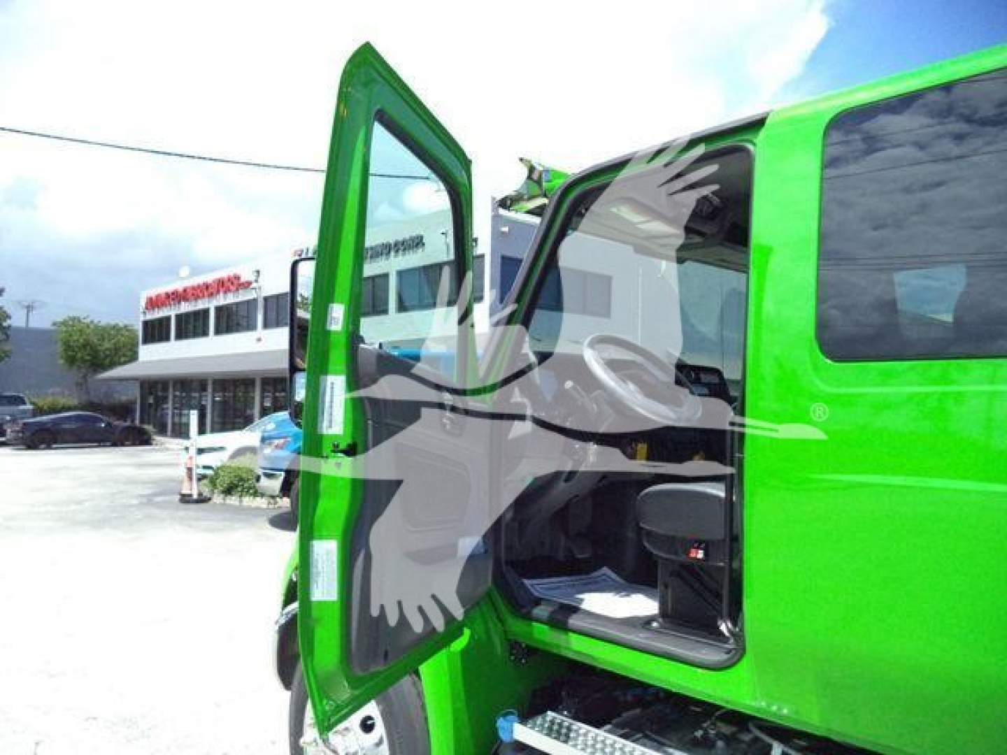 Green truck cab with side door open showing interior seating and dashboard. Background shows dealership lot and other vehicles.