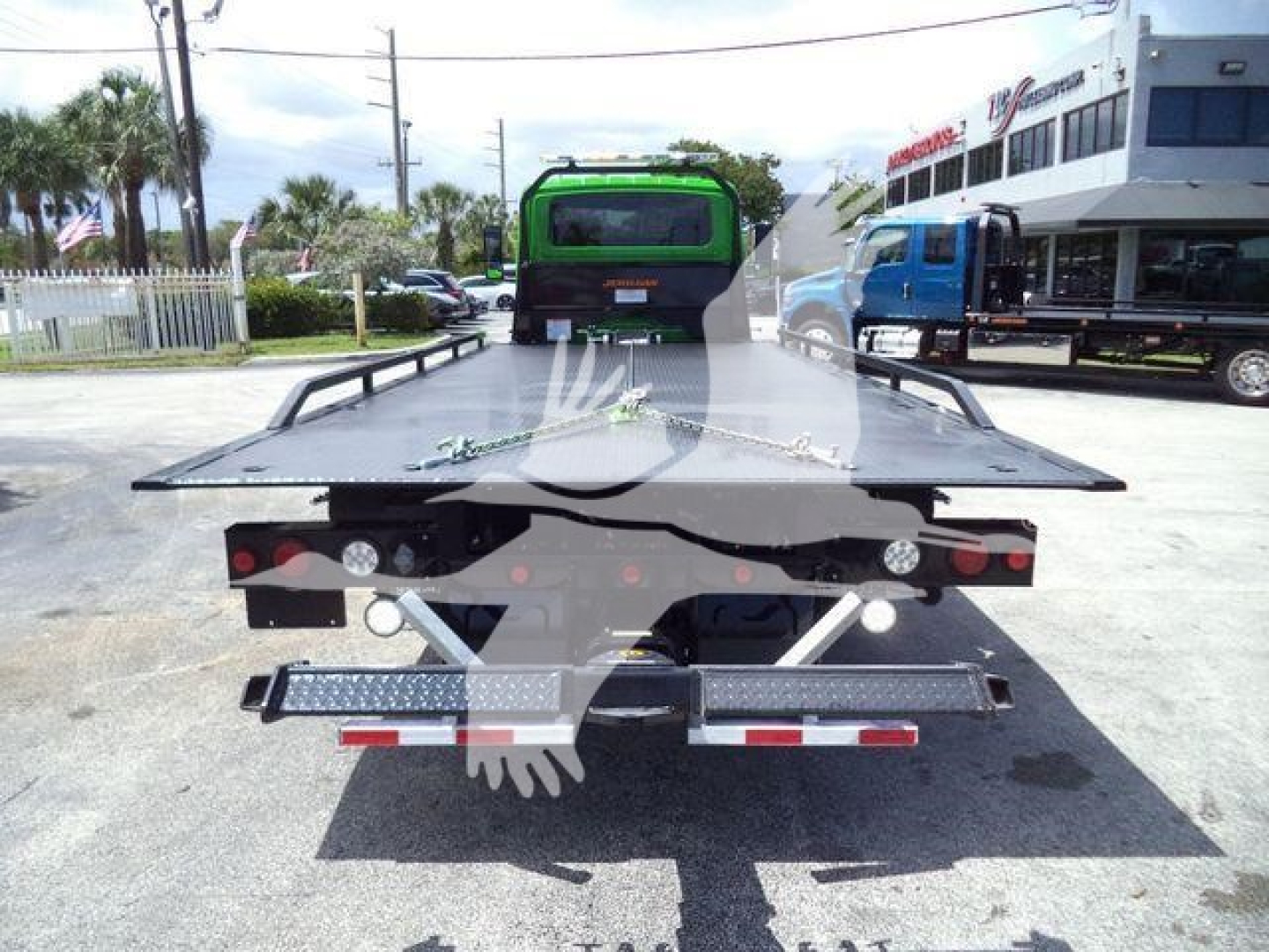 Flatbed rollback tow truck rear view showing tail lights, bumper, and wheel chocks.