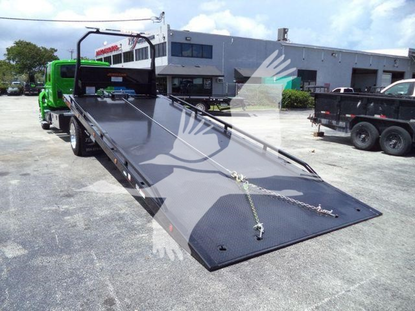 International MV rollback truck showing a long flatbed loading ramp with chain tie-downs.