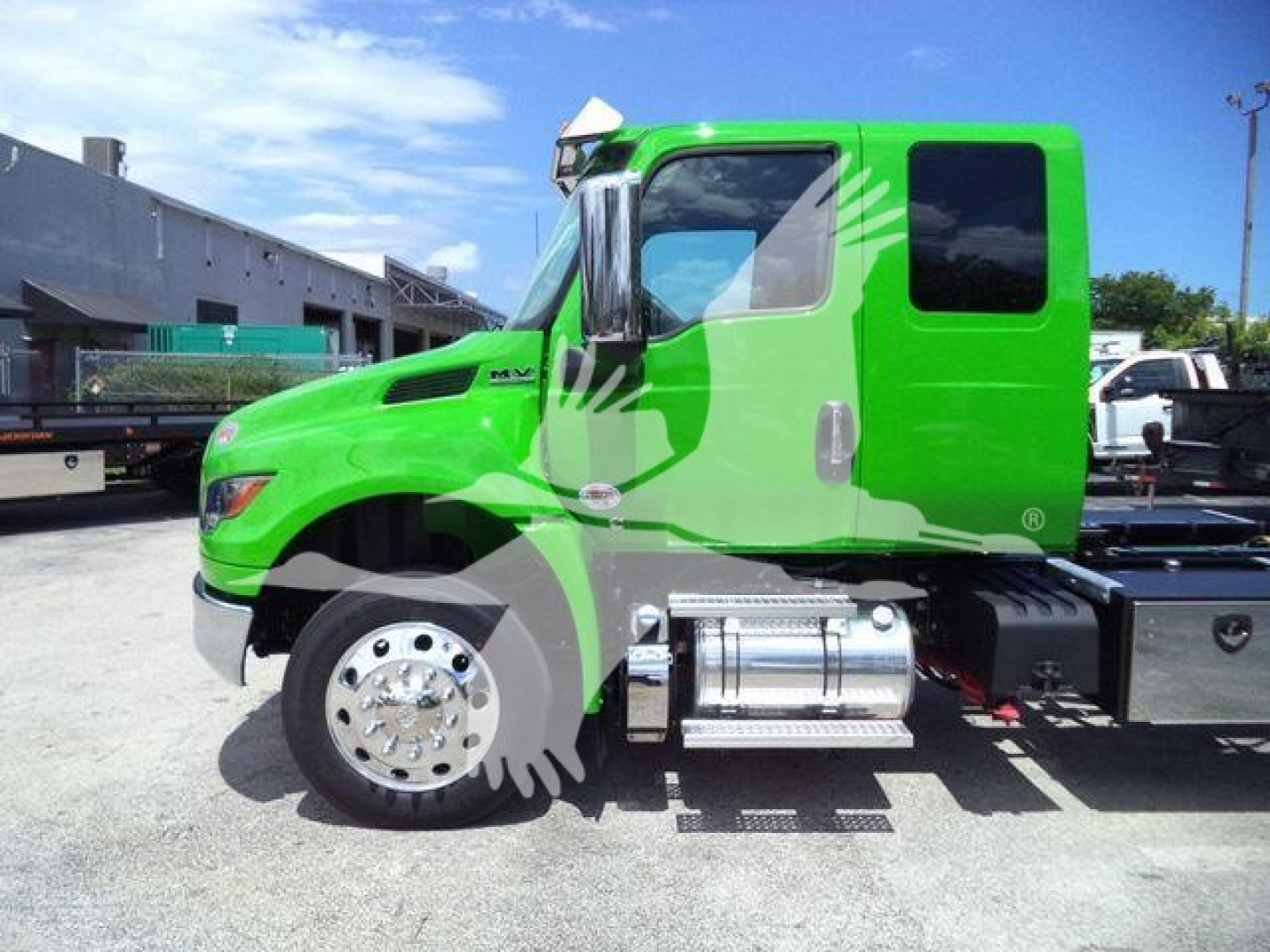 Green International MV truck cab side view with chrome fuel tanks and black chassis, 'MV' badge on door, clear sky