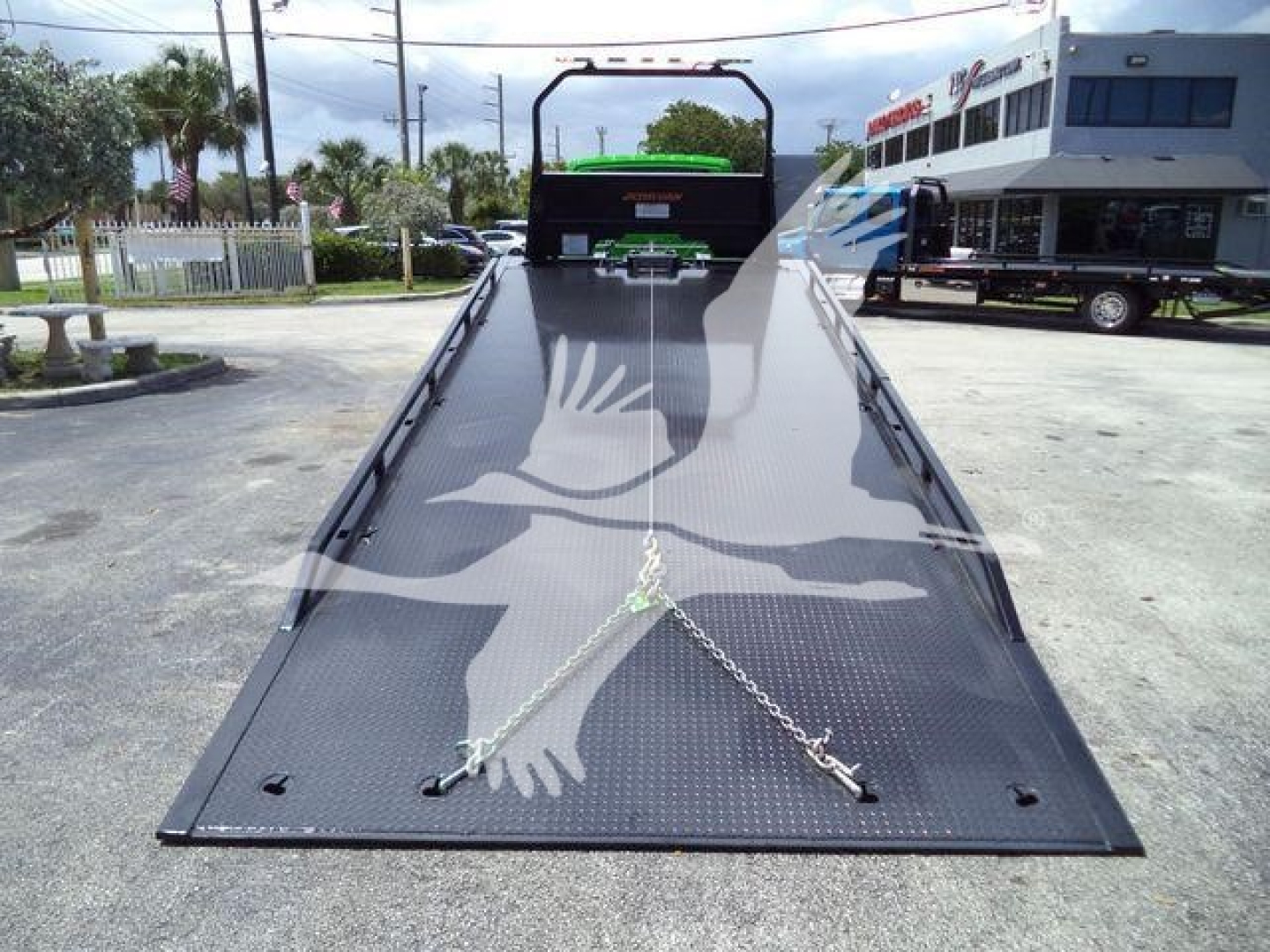 2017? 2027 International MV rollback truck bed in open lot showing tie-down chains and ramps, with dealership building in background.