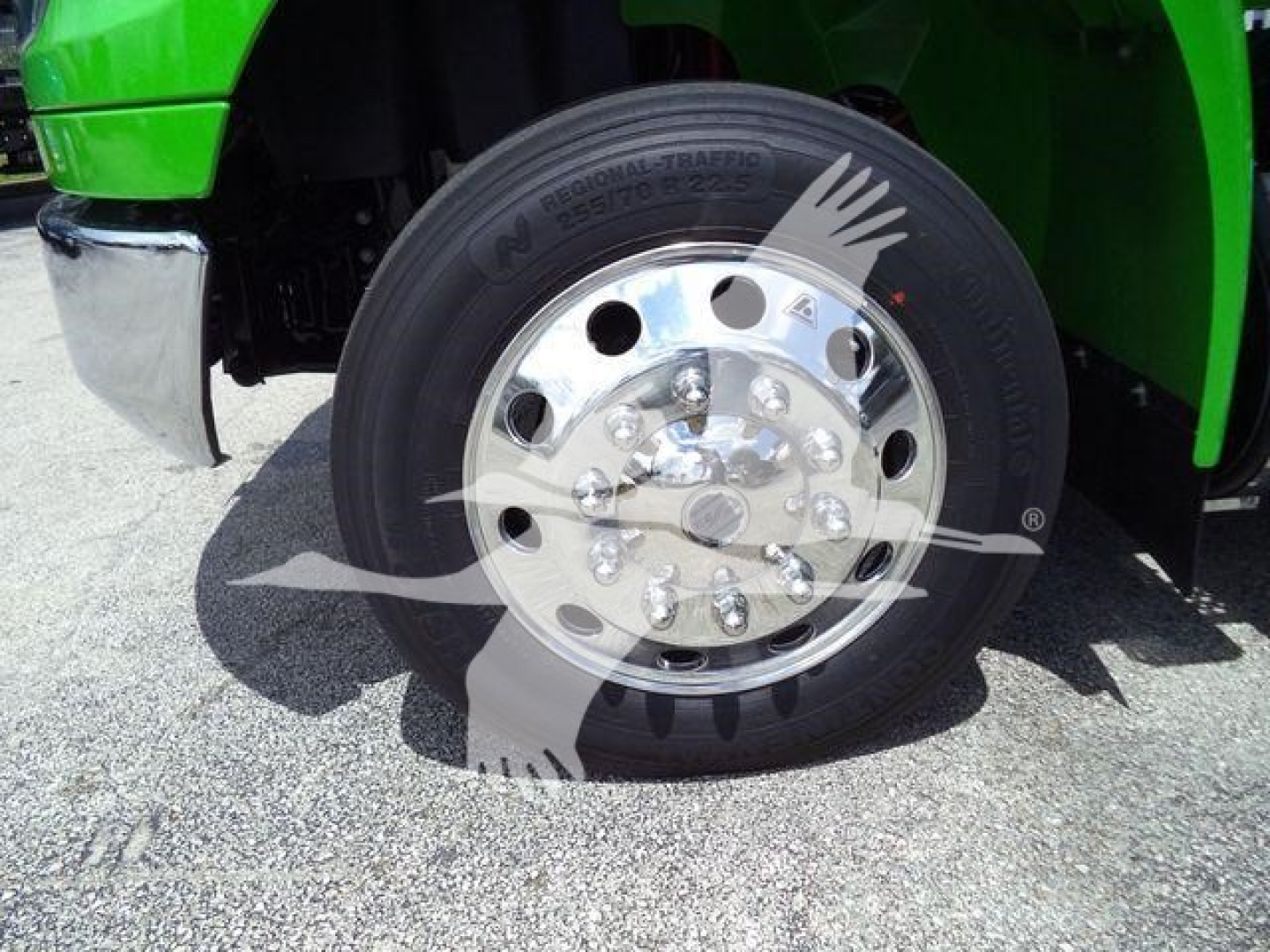 Wheel and front fender of a bright green International MV truck showing polished aluminum hubcap and Goodyear tire.