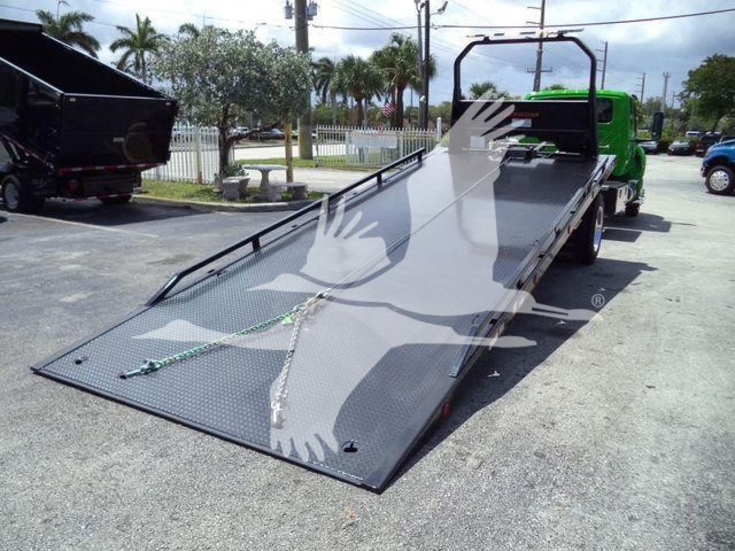 Truck rollback flatbed with green cab showing metal ramp surface and straps.