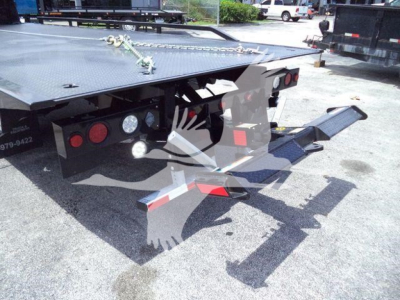 Flatbed rollback trailer showing rear ramp and taillights with chains and reflective markings.