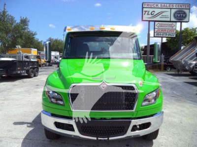 Green International MV truck in a dealership lot front view with chrome grille, bumper, and truck signs in background.