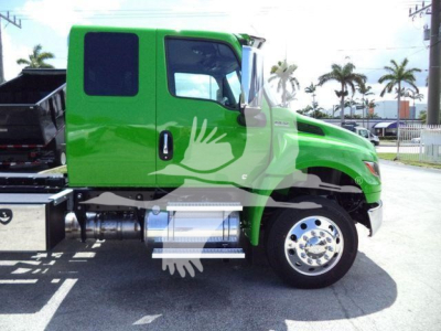 Green International MV truck side profile showing cab with large window, chrome fuel tanks under door, and reflective wheel hub; palm-tree background.