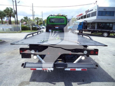 Tow truck flatbed rollback showing rear view with ramps and hitch fittings, black flatbed with red/white reflective tape.