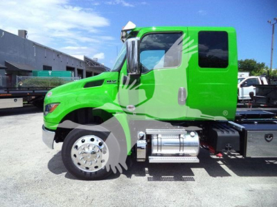 Green International MV truck cab side view with chrome fuel tanks and black chassis, 'MV' badge on door, clear sky