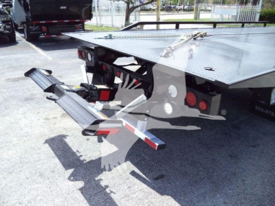 Trailer hitch/rollback tow equipment mounted on a flatbed truck with a rear platform and loading ramps visible.