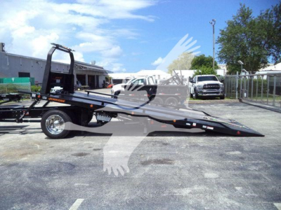 Truck bed rollback tow truck on trailer with ramp and winch in an outdoor lot.