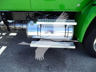 Truck fuel tank and side steps on a green International MV truck; chrome cylindrical fuel tank with perforated metal steps above and below; visible drivetrain components.