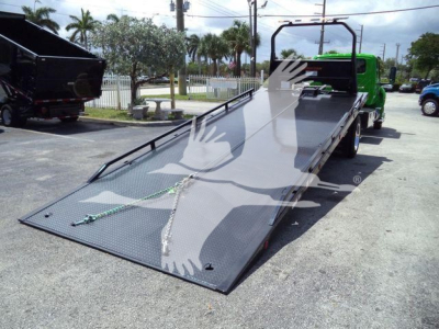 Truck rollback flatbed with green cab showing metal ramp surface and straps.