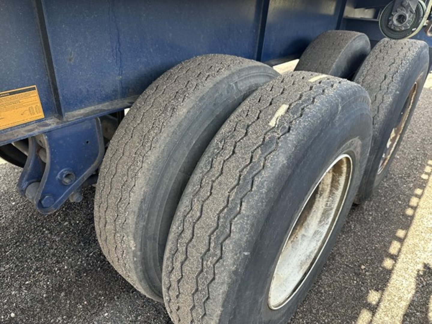 Tandem axle trailer wheels and blue steel frame showing two rear dual tires with wear and wheel rims.