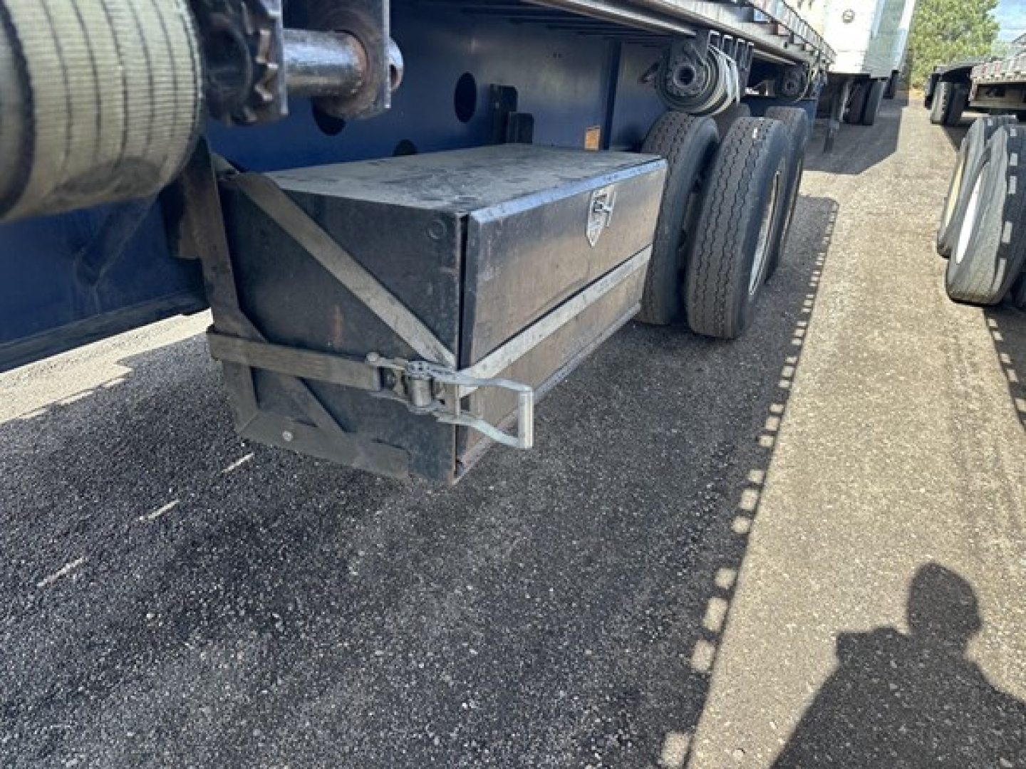 Trailer undercarriage showing a mounted metal toolbox and wheel group, 45' steel closed tandem flatbed with forklift kit storage box.