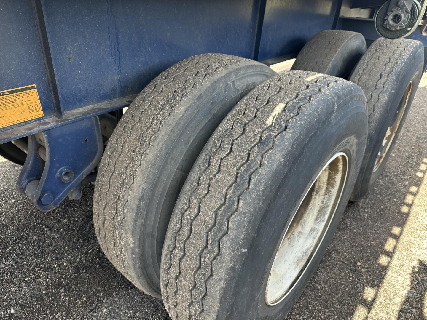 Flatbed trailer tandem axle tires and wheel wells showing wear, blue body, and fork lift kit attachment area.