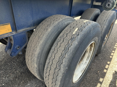Flatbed trailer tandem axle tires and wheel wells showing wear, blue body, and fork lift kit attachment area.