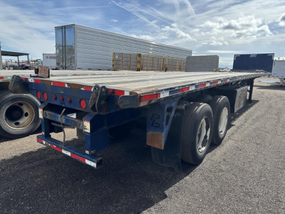 Flatbed trailer showing triple-axle rear end and wooden deck with spare wheel wells; blue chassis, red-and-white reflective tape, rear lights and bumper.
