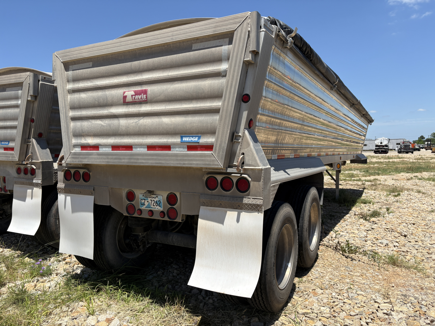 Dump trailer rear view showing Travis logo, aluminum side walls, dual rear axles with mud flaps, and taillights.