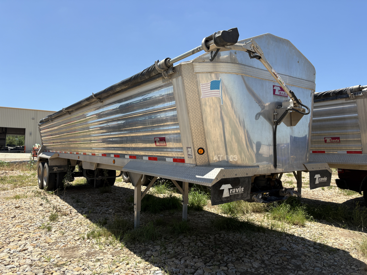 Trailer side view showing aluminum dump trailer with Travis branding and a front/tint cap.
