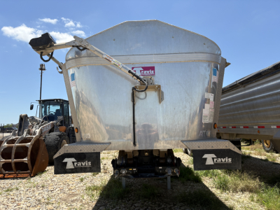 Back view of a Travis dump trailer showing the tail area, with black fenders labeled ‘Travis’ and a metal tailgate, with a hydraulic arm on the left side.
