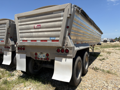 Dump trailer rear view showing Travis logo, aluminum side walls, dual rear axles with mud flaps, and taillights.